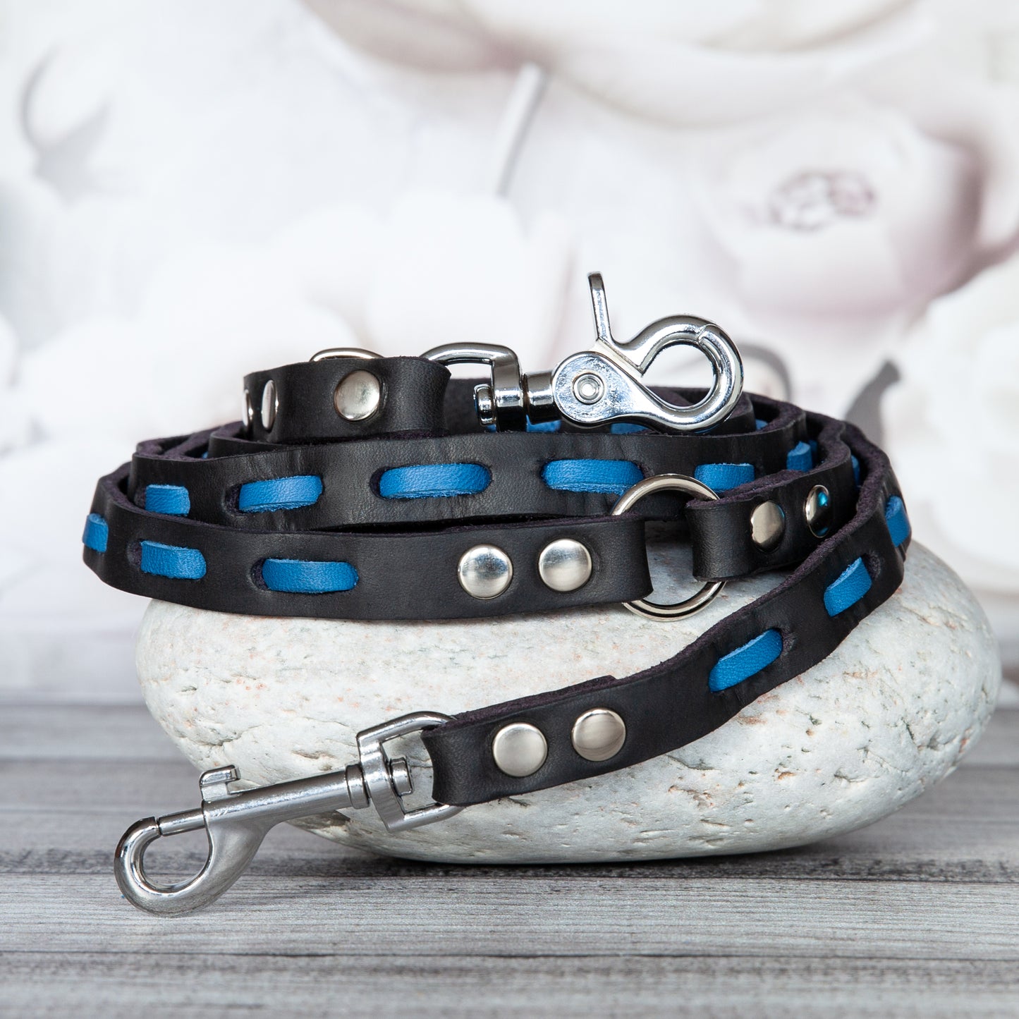 Handgefertigte Hundeleine Lily aus schwarzem Premiumleder mit azurblauem Lederelement und silberfarbenem Karabiner, stilvoll auf Naturstein präsentiert.