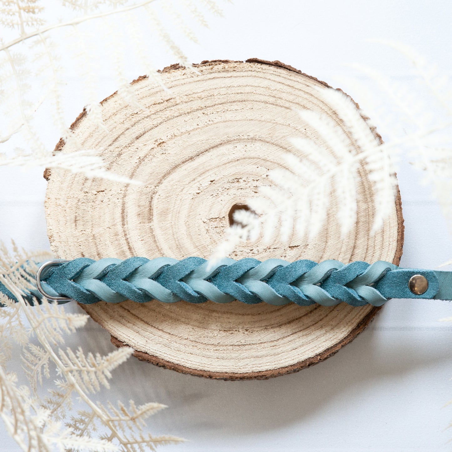 Detailansicht des Halsbands MILA in Eisblau – kunstvoll geflochtenes Leder mit zarter Struktur, liebevoll präsentiert auf hellem Holz.