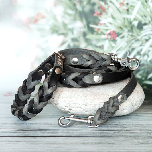 Geflochtenes Hundeleinen- und Halsband-Set Sue in Grau-Schwarz aus handgefertigtem Leder mit silberfarbenem Karabiner, dekorativ auf Stein präsentiert.